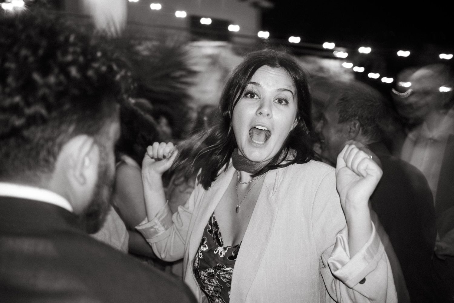 A guest dances enthusiastically at a festive outdoor party under string lights.