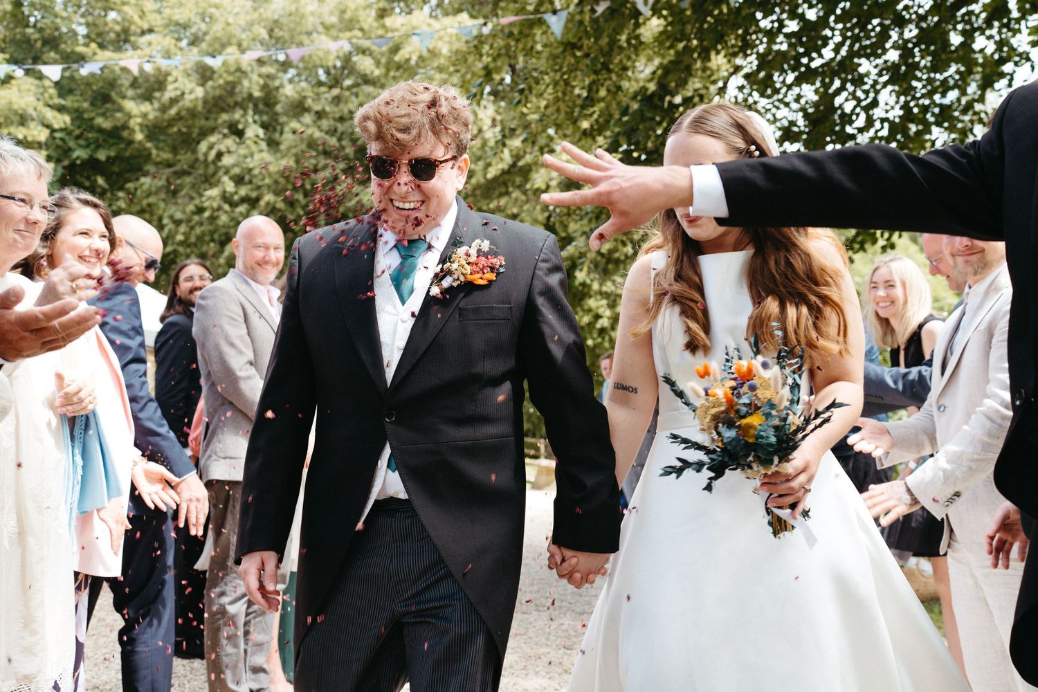A joyful outdoor celebration with confetti being thrown at a festive countryside wedding.