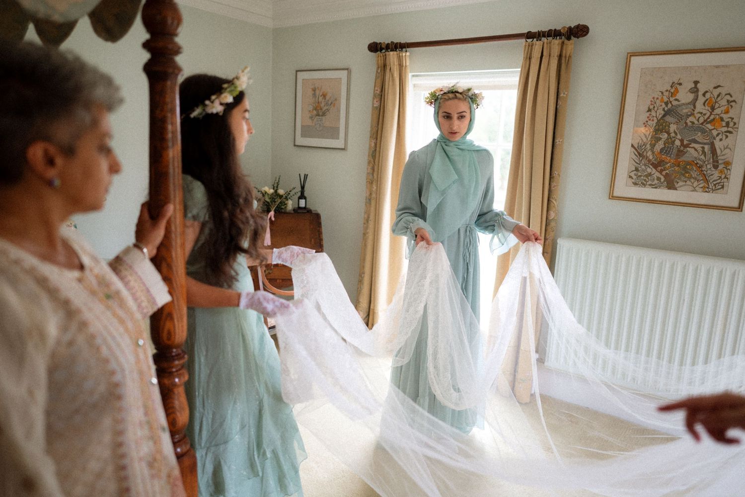 Wedding party admiring a flowing white dress in an elegant bedroom during pre-ceremony preparations.