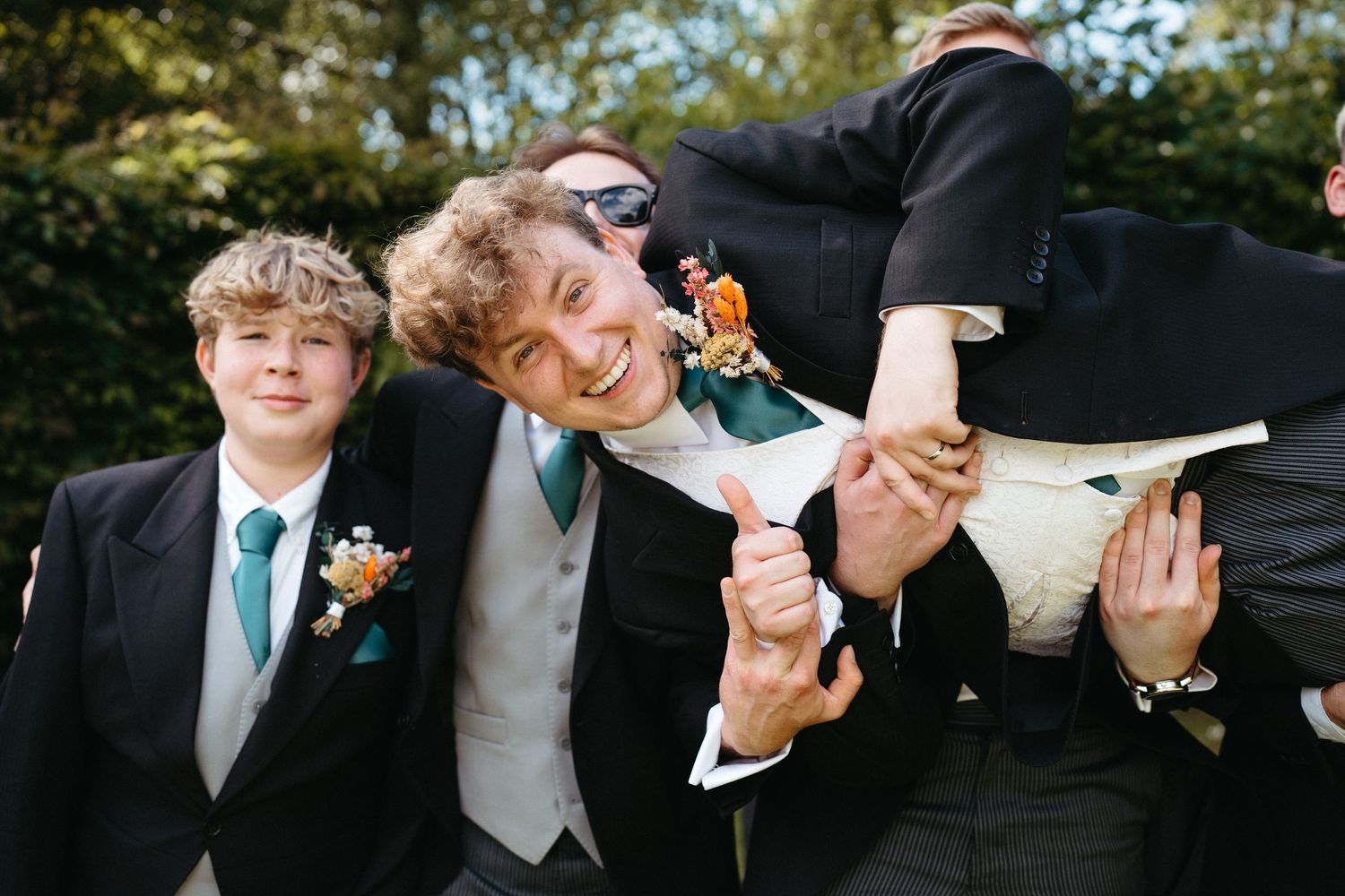 Joyful group in formal wear laugh and play around together at an outdoor celebration.