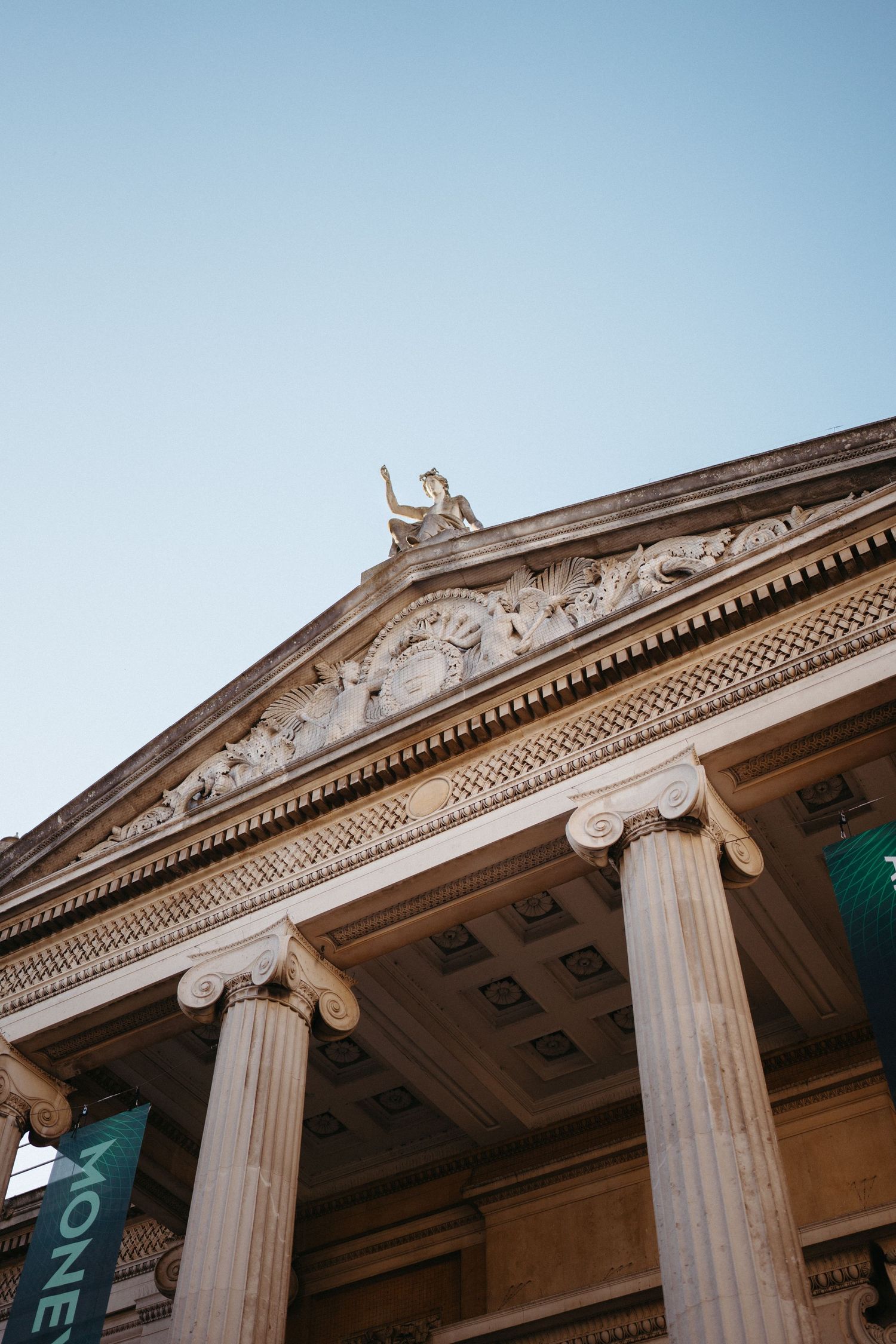 Low angle view of neoclassical building facade with Ionic columns against blue sky.