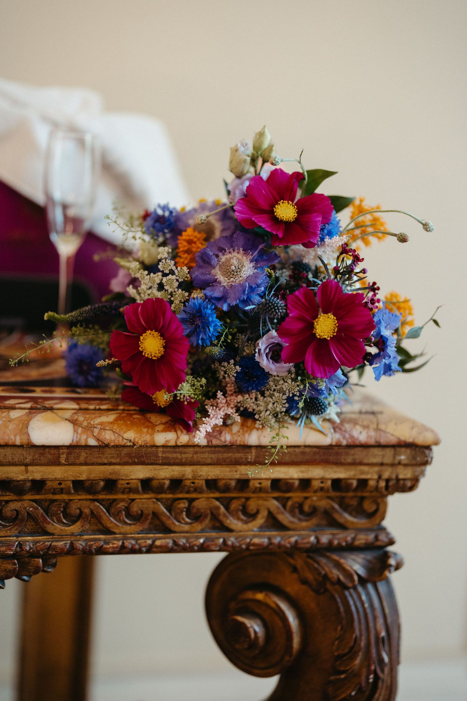 Vibrant wildflower bouquet with pink cosmos and blue blooms on an ornate antique table.