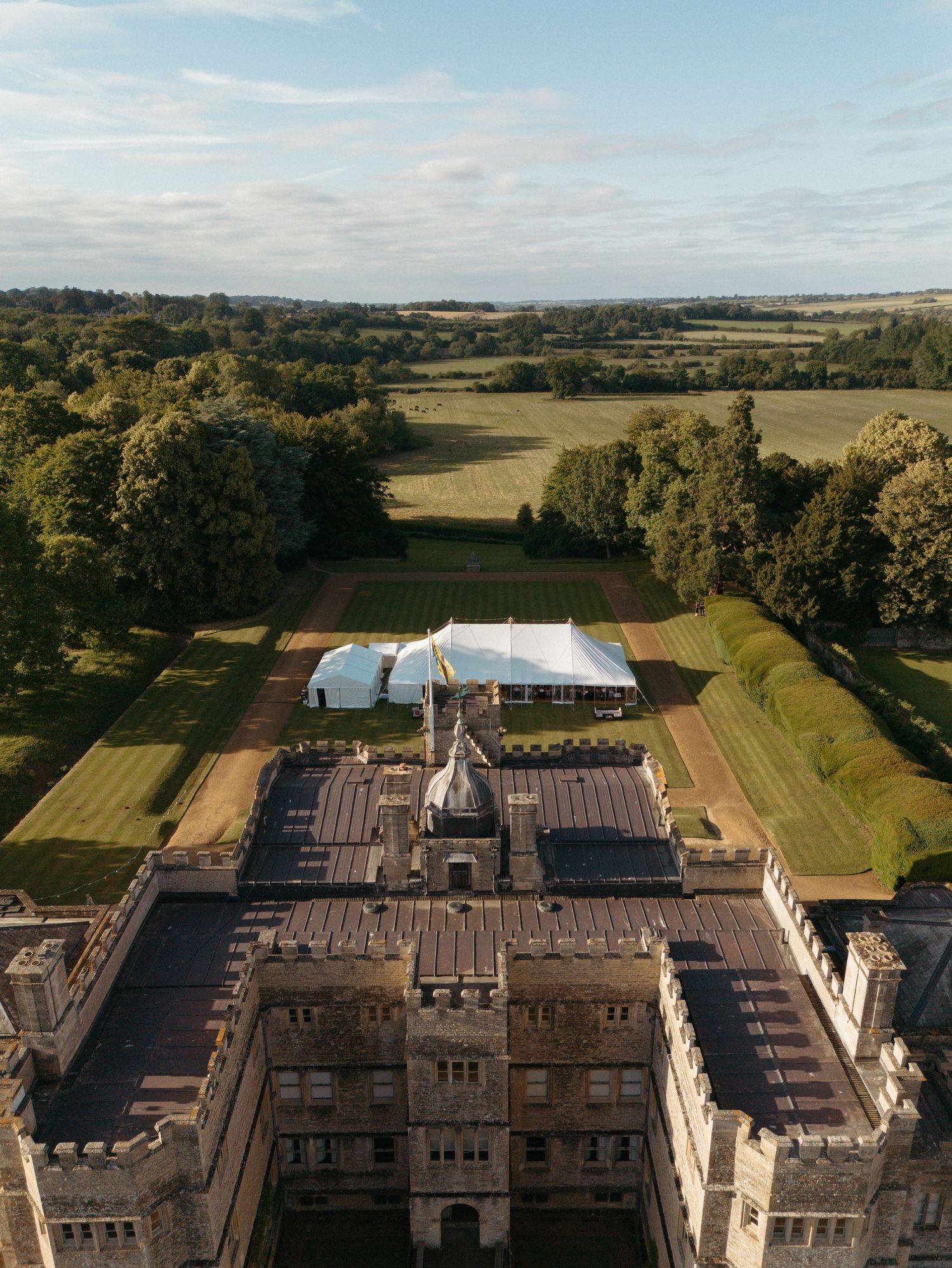 Aerial view of a grand castle with a white event tent and perfectly manicured grounds.