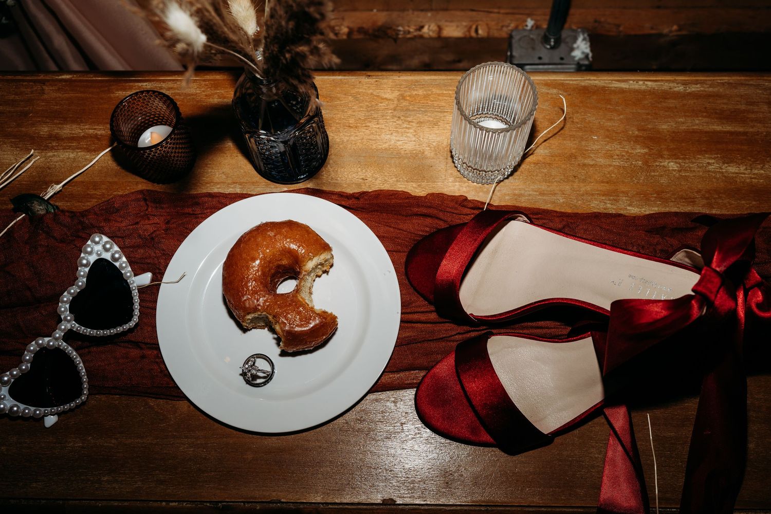Overhead view of a croissant on white plate with red ballet flats and heart-shaped sunglasses on wooden table.