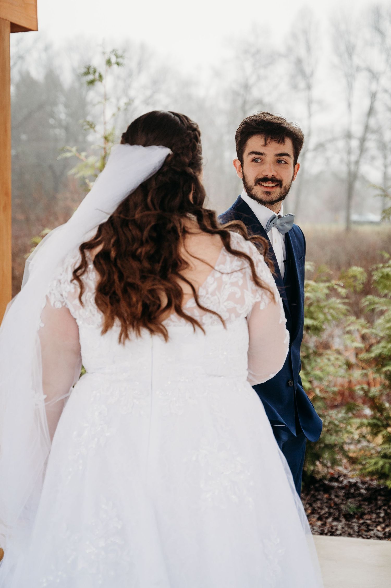 A romantic wedding moment captured during a misty outdoor ceremony with the bride wearing a lace gown with long sleeves.
