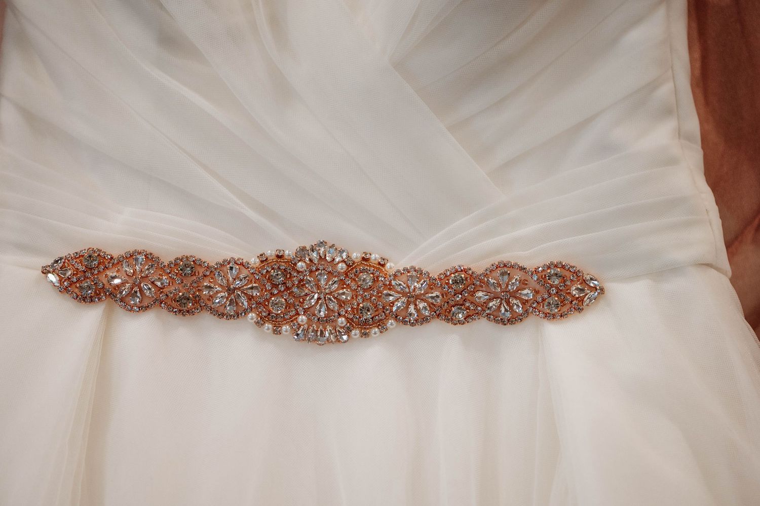Rose gold rhinestone crystal beaded sash adorns a white tulle wedding dress.