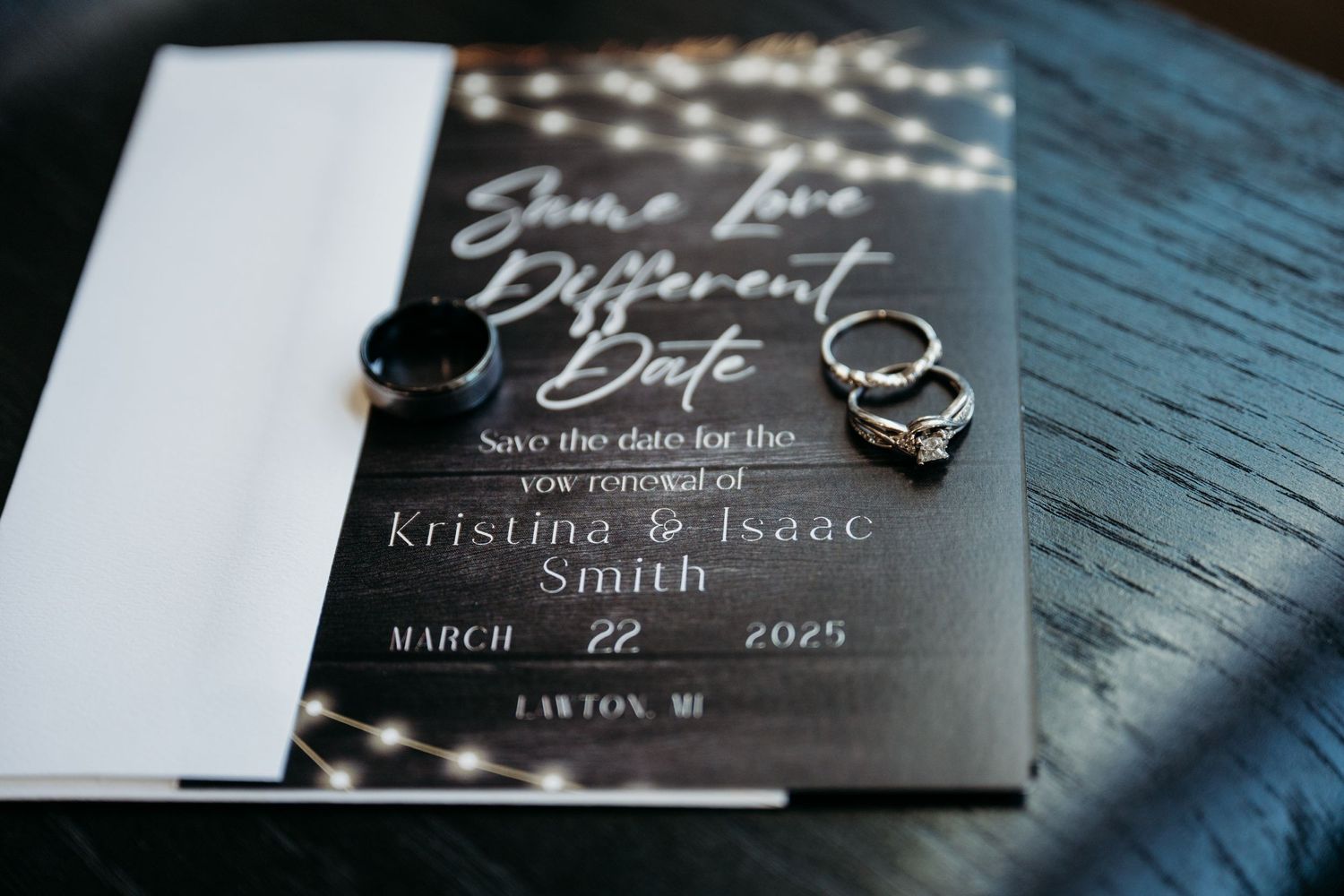 Elegant black and white wedding invitation with rings on a textured blue surface.