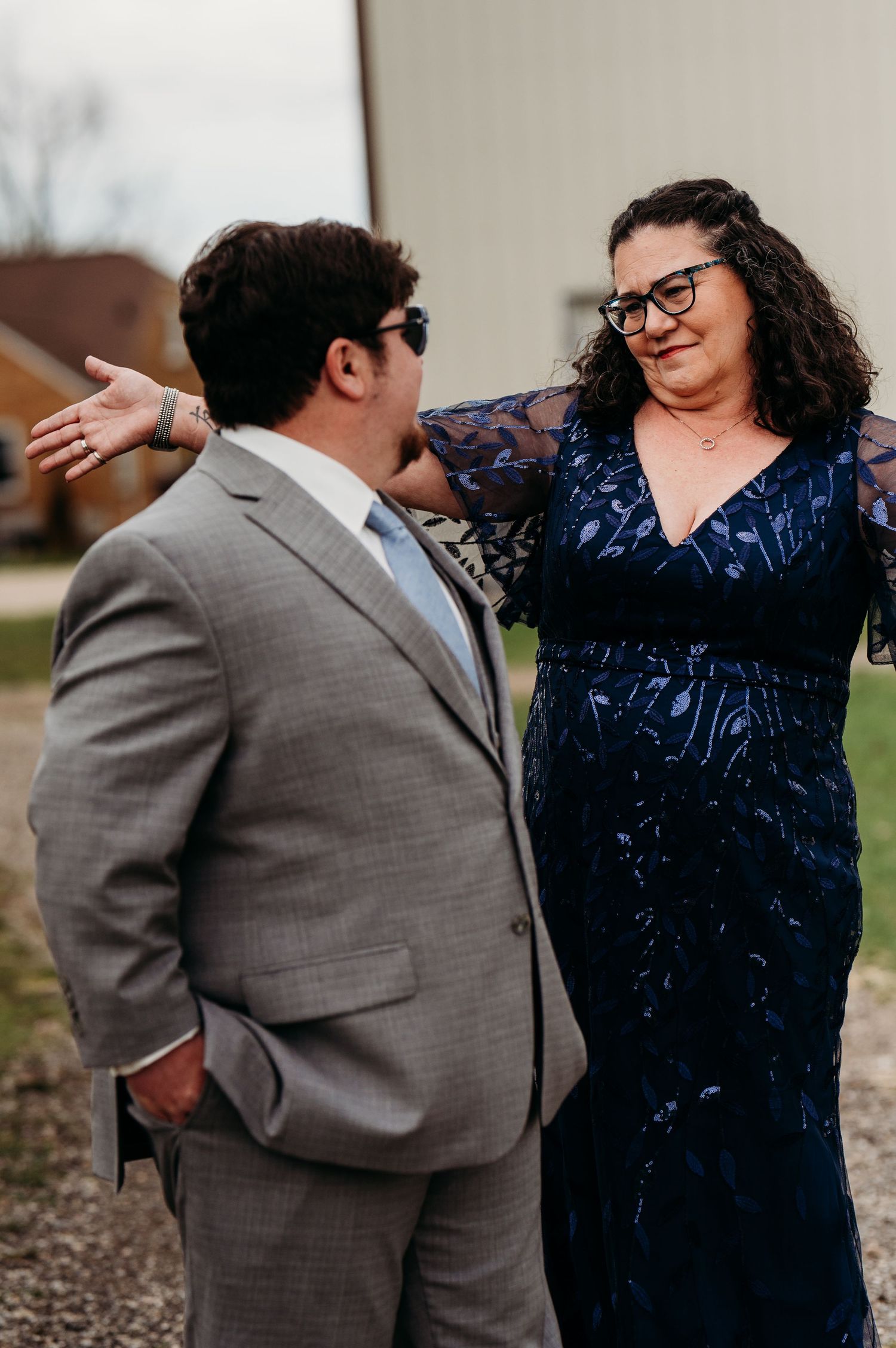A couple in formal attire shares a joyful moment outdoors, with one wearing a gray suit and the other in a navy dress.