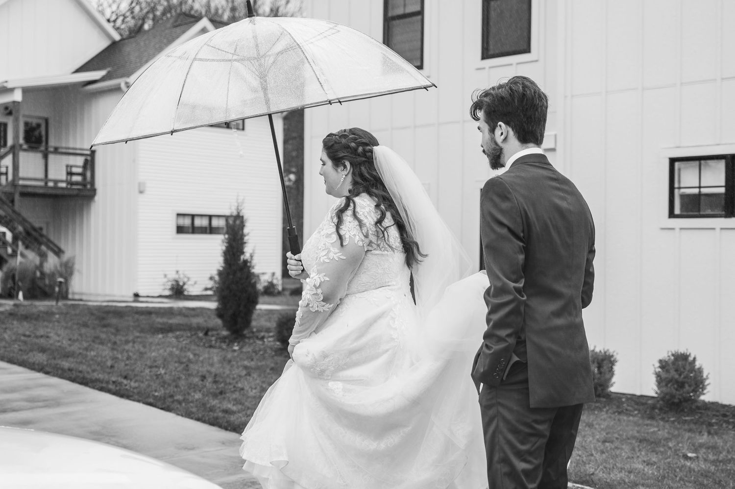A groom holds a white umbrella over his bride in an intimate black and white wedding photograph.