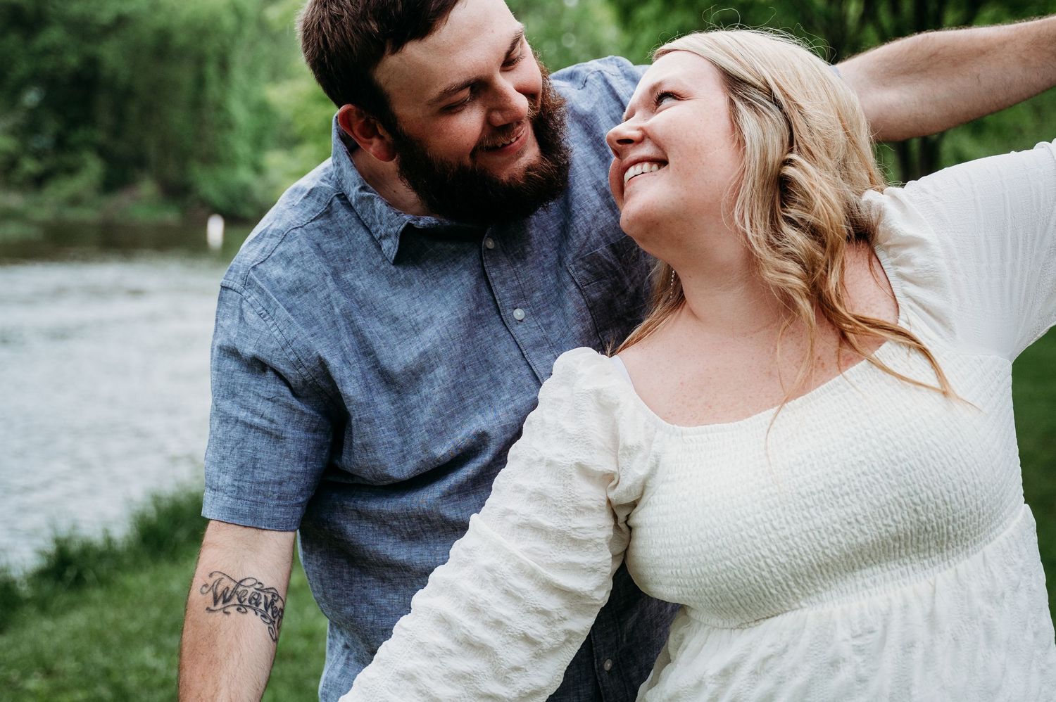 A joyful couple shares a candid moment of laughter while sitting together outdoors in casual attire.