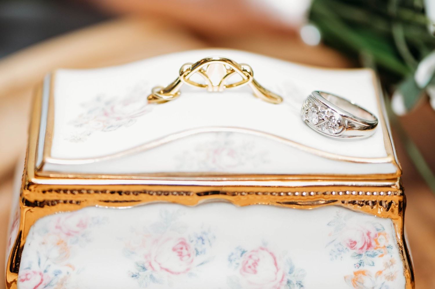 Wedding rings displayed on an ornate white and gold porcelain box decorated with delicate floral patterns.