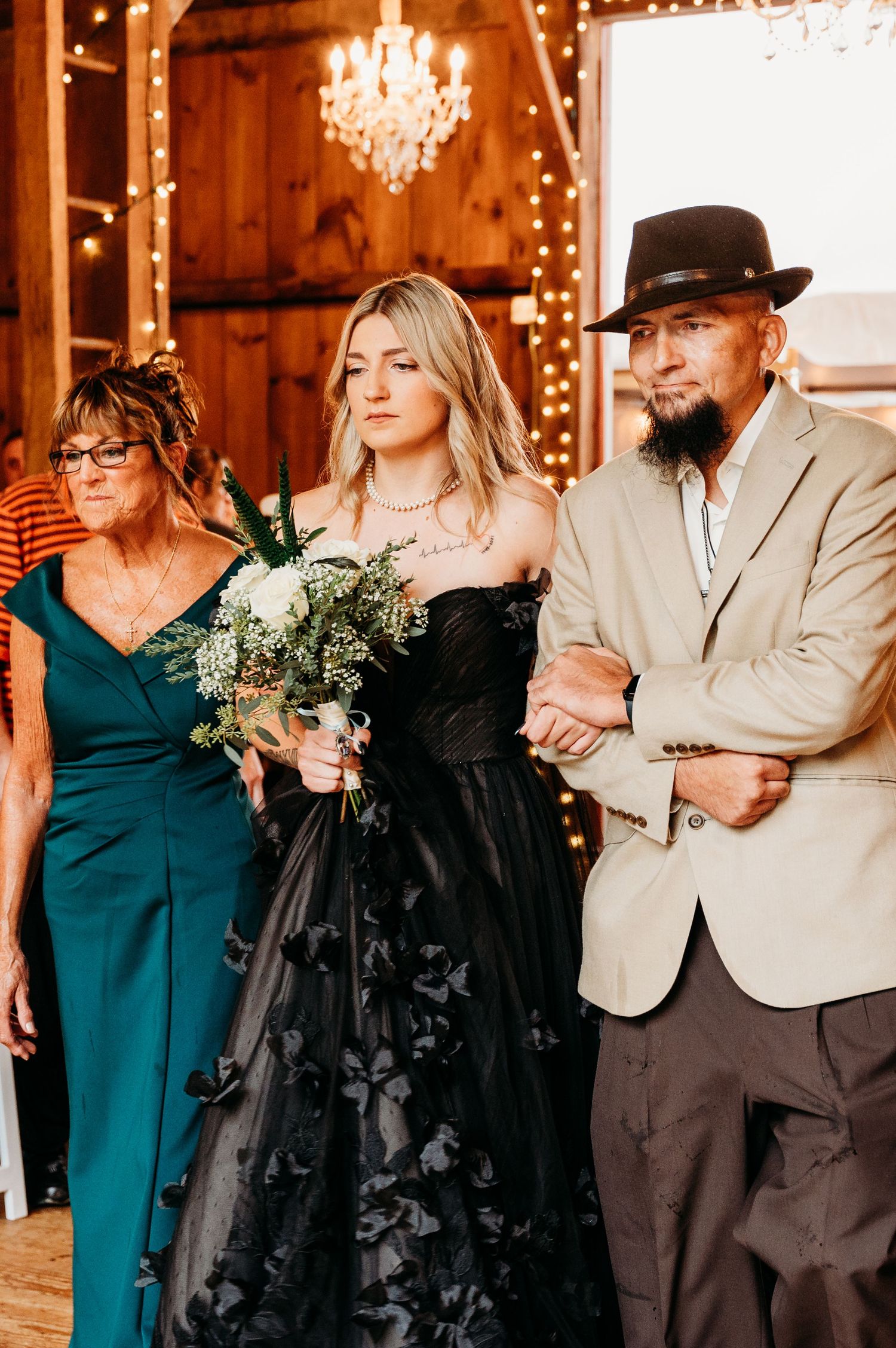 A group in formal attire poses at a barn wedding with a woman in a black gown holding a bouquet.