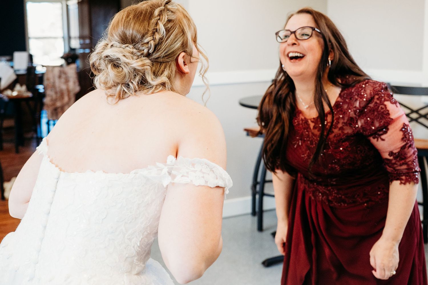 A joyous candid moment between friends sharing laughter at what appears to be a wedding reception.