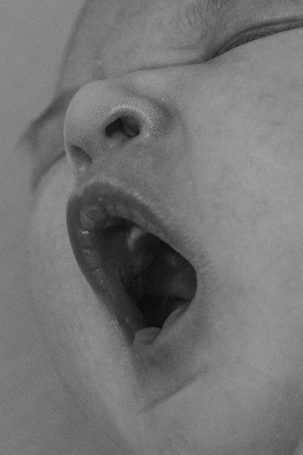 A black and white close-up photograph shows an open mouth and nose in soft focus against a light background.