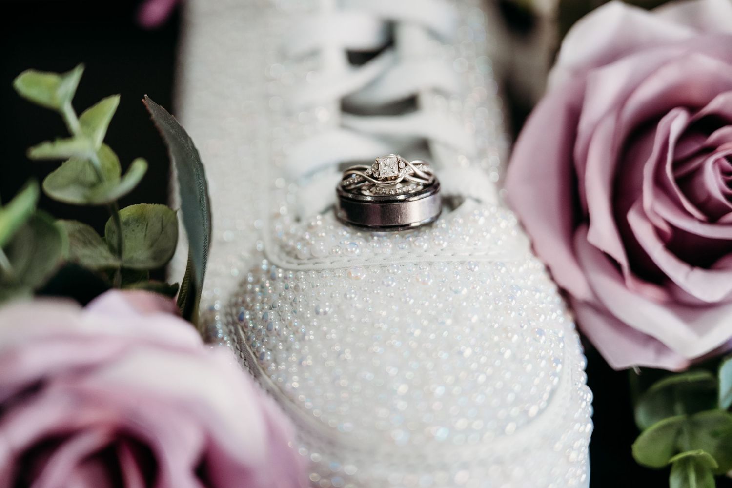 Wedding rings displayed on white textured decor with pink roses and greenery in elegant arrangement.