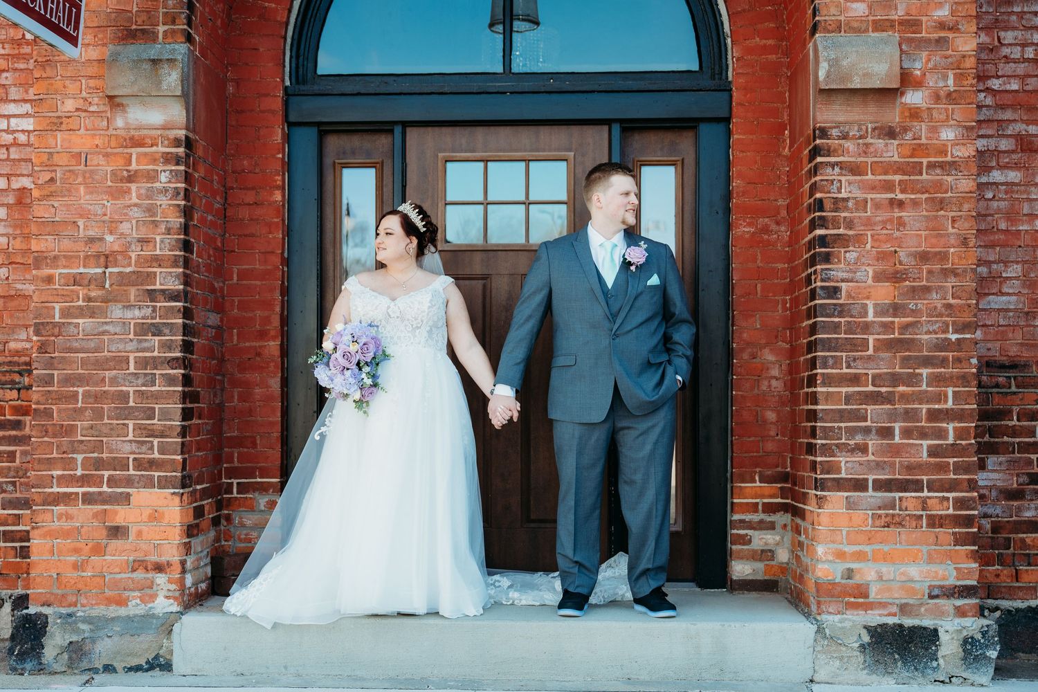 A romantic wedding couple stands together in a brick archway entrance with turquoise trim on their special day.