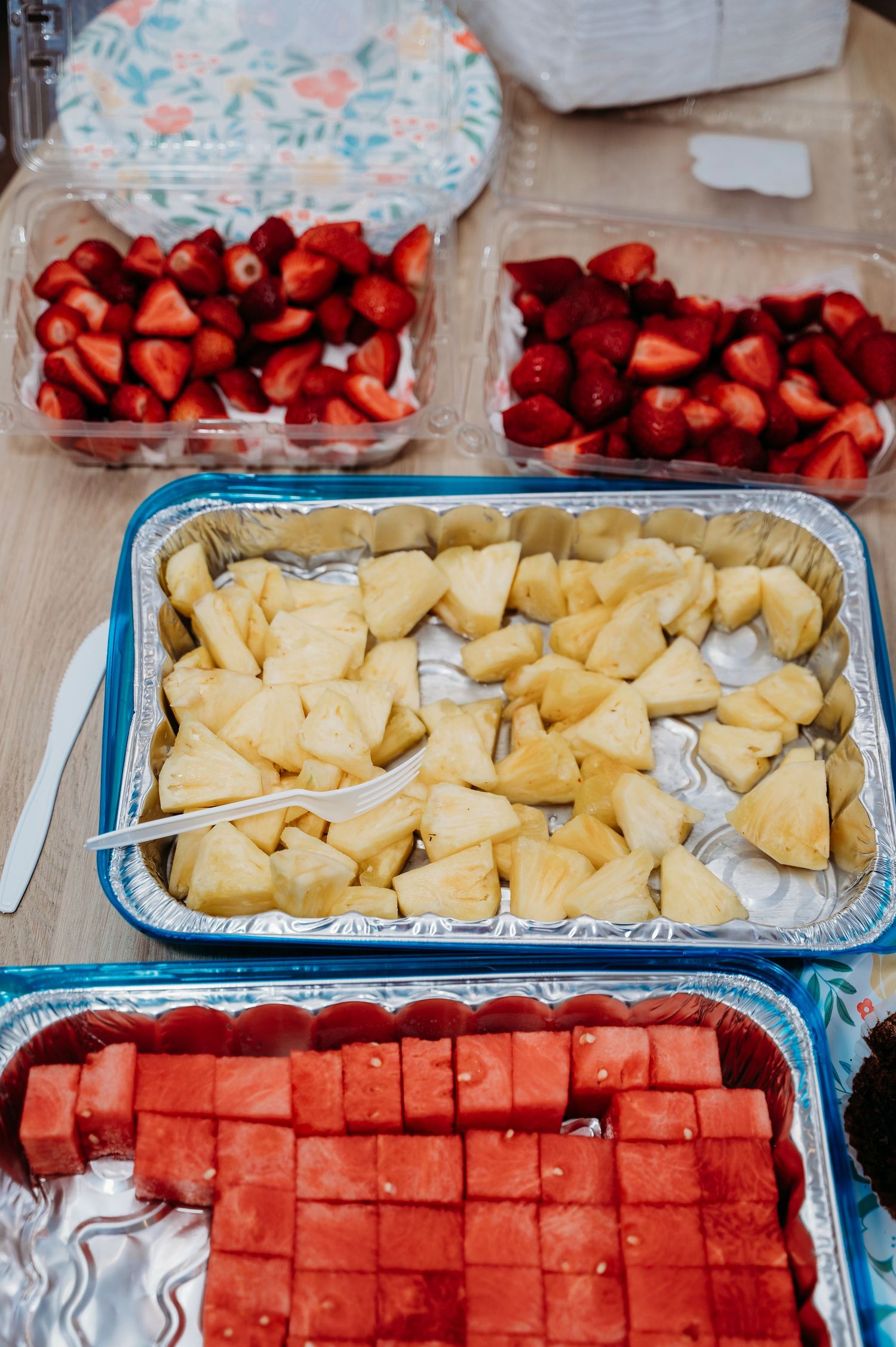 Fresh cut fruit spread with sliced pineapple, watermelon cubes, and bright red strawberries in serving trays.