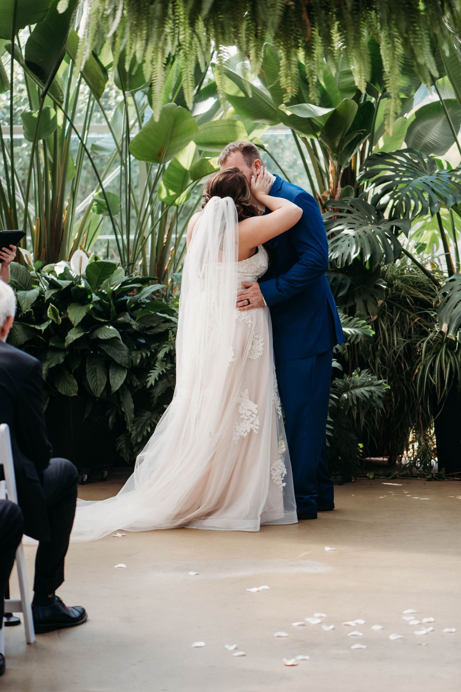 A romantic wedding ceremony moment with a couple embracing under lush tropical greenery and palm fronds.