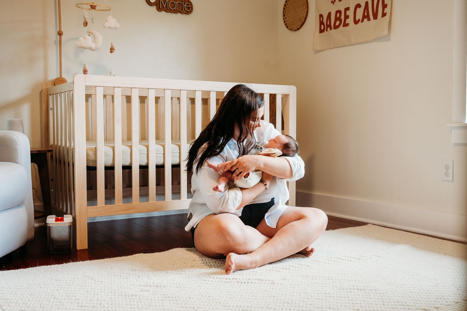 Tender family moment captured in nursery with white crib as siblings gather around new baby in warm natural light.