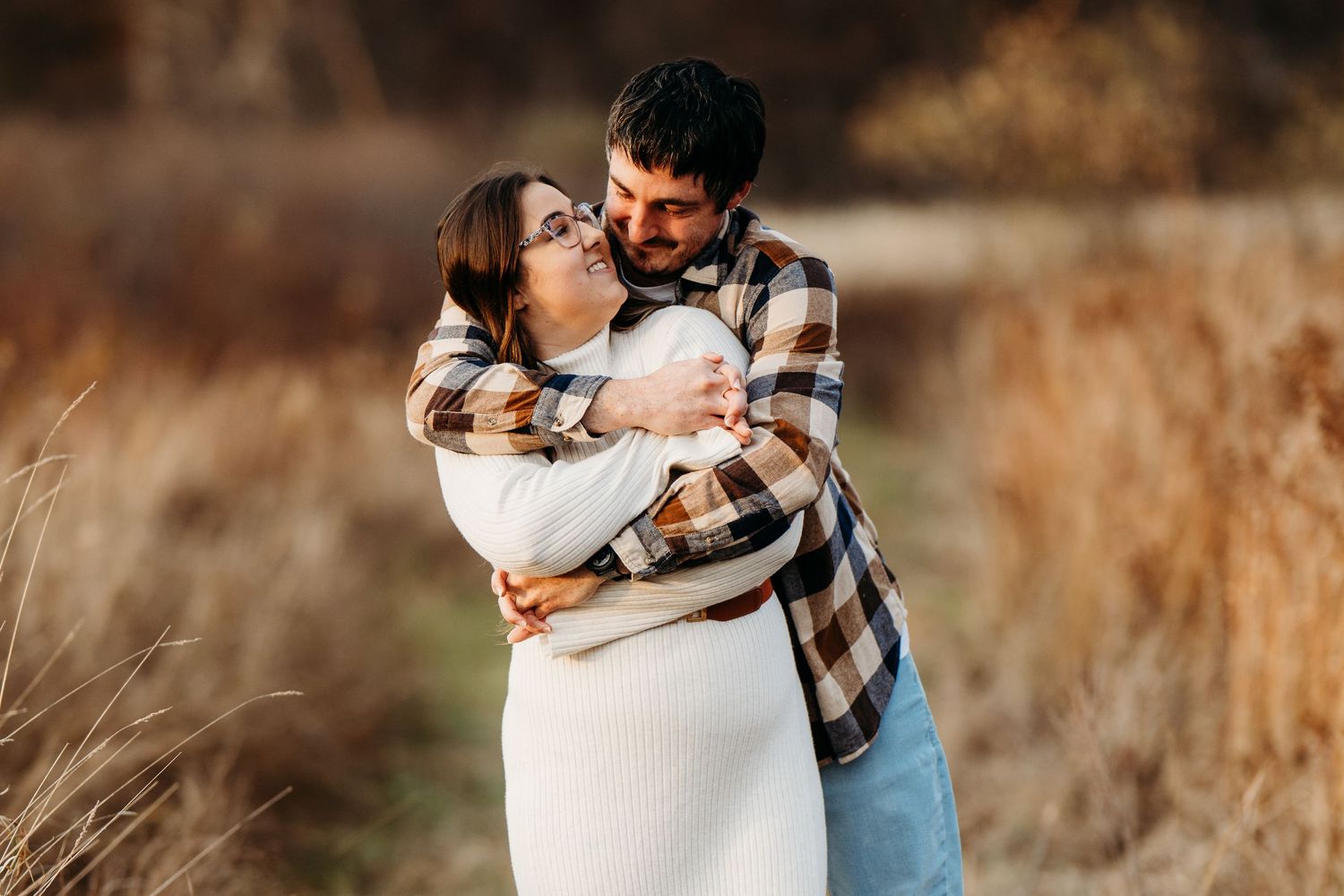 Romantic autumn portrait of couple embracing in tall brown grass during golden hour sunset.
