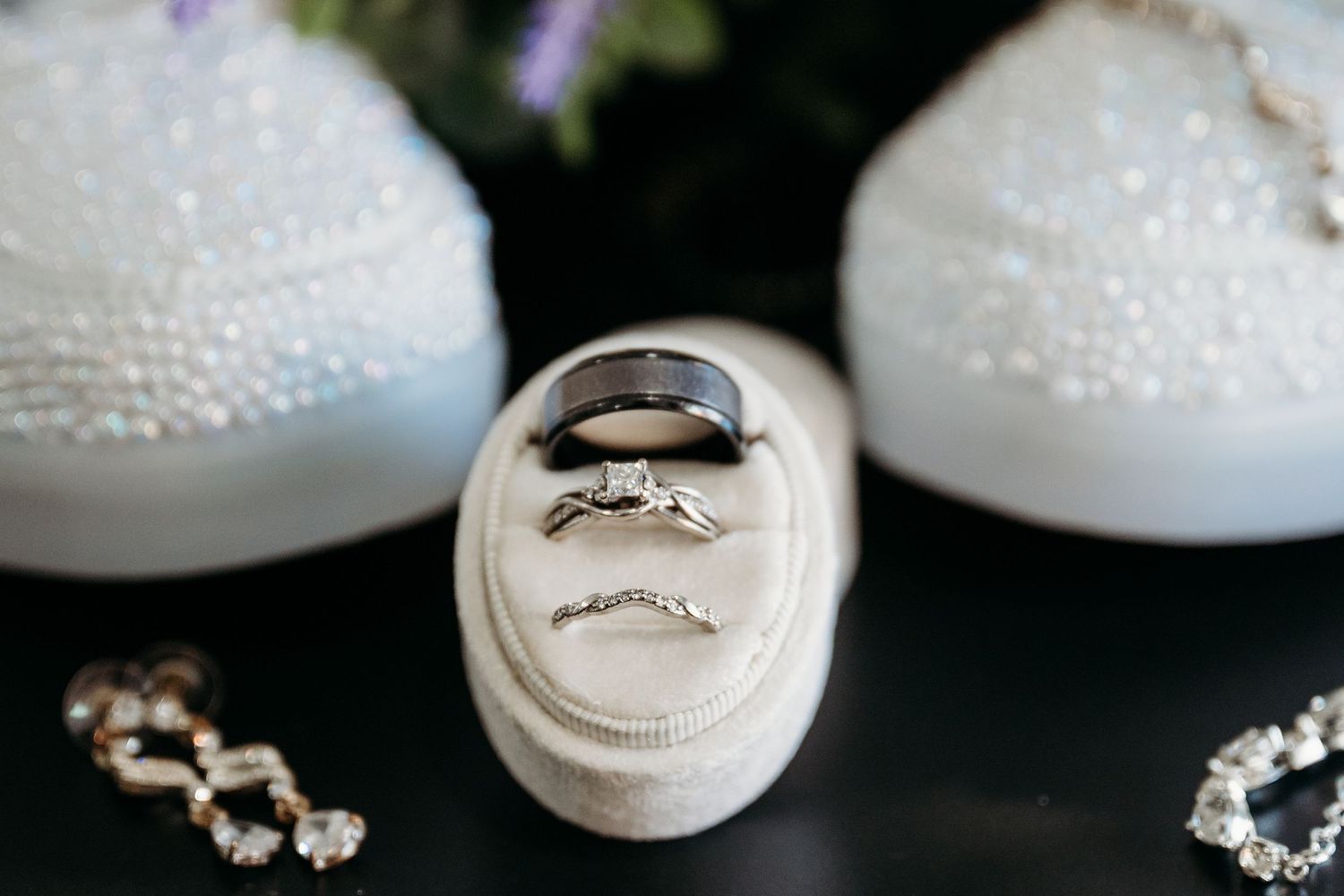 Wedding rings nestled in an elegant white ring holder with delicate pearl details and sparkly jewelry accents.