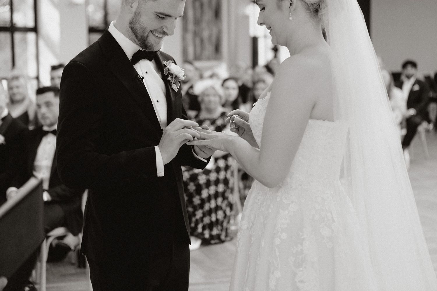 A tender moment at a wedding ceremony where a couple exchanges rings in an elegant black and white setting.