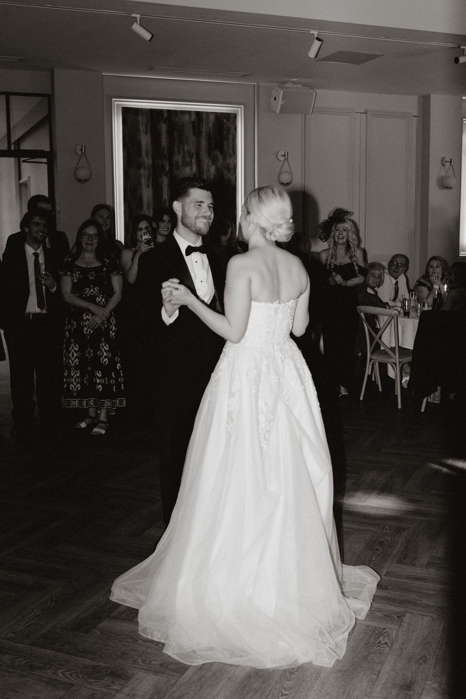 A couple shares their first dance at a wedding reception, the bride wearing a flowing white strapless gown.