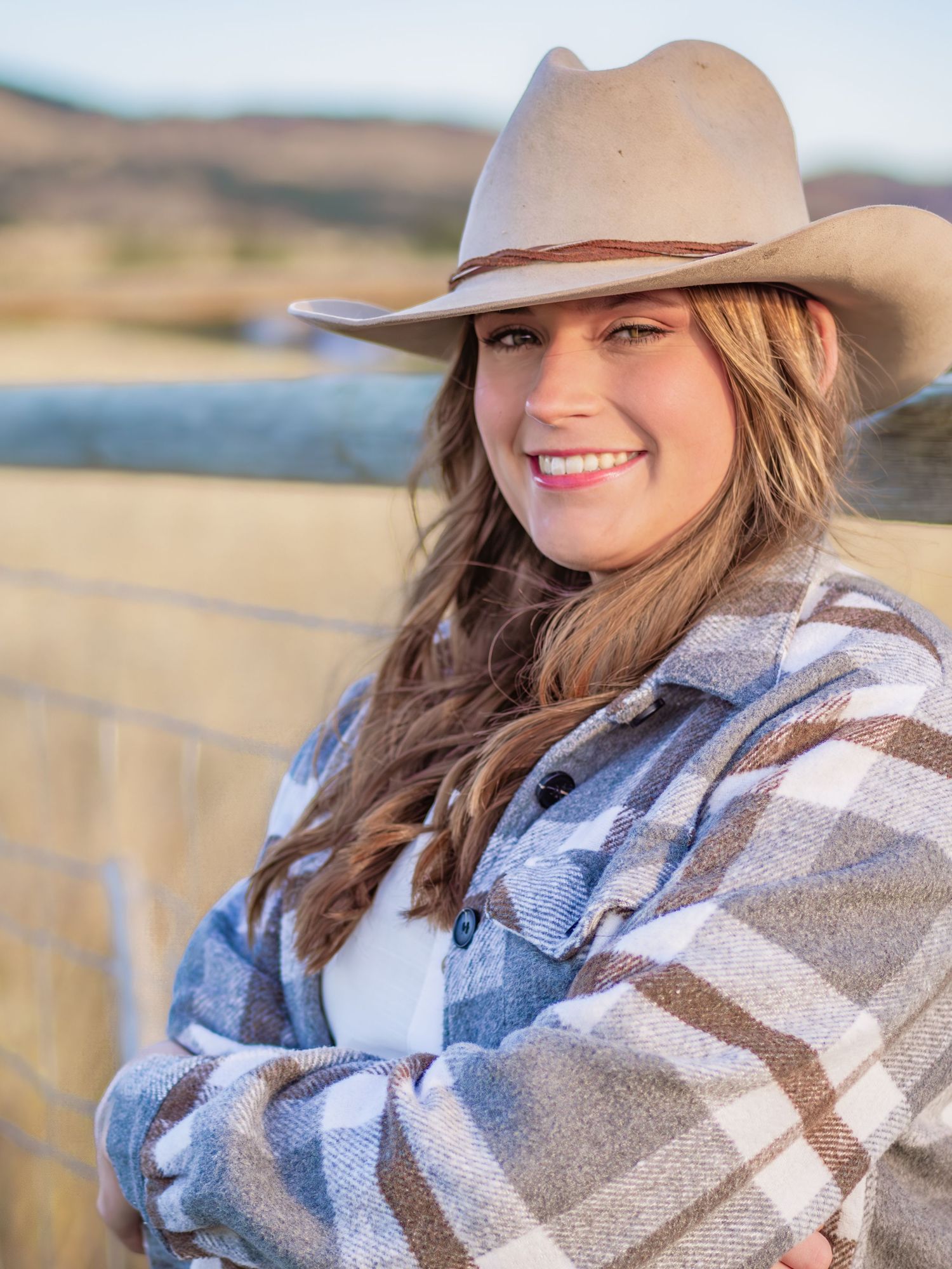 Someone in a cowboy hat and plaid flannel jacket against a scenic backdrop.