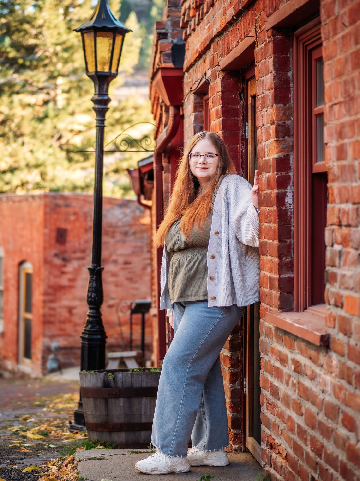 Someone in casual attire leaning against a brick building with a vintage lamp post.