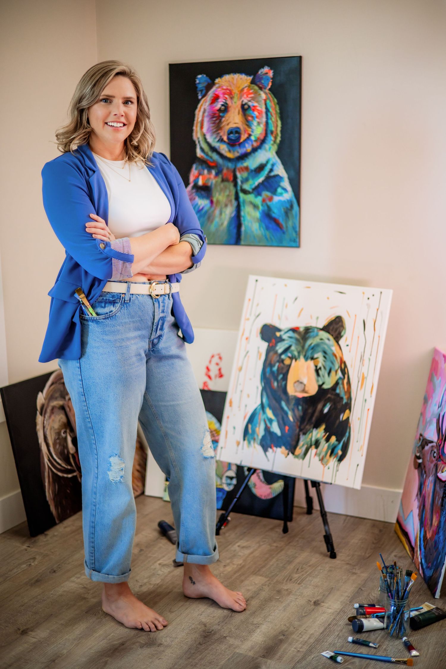 Artist standing beside colorful bear paintings in home studio space.