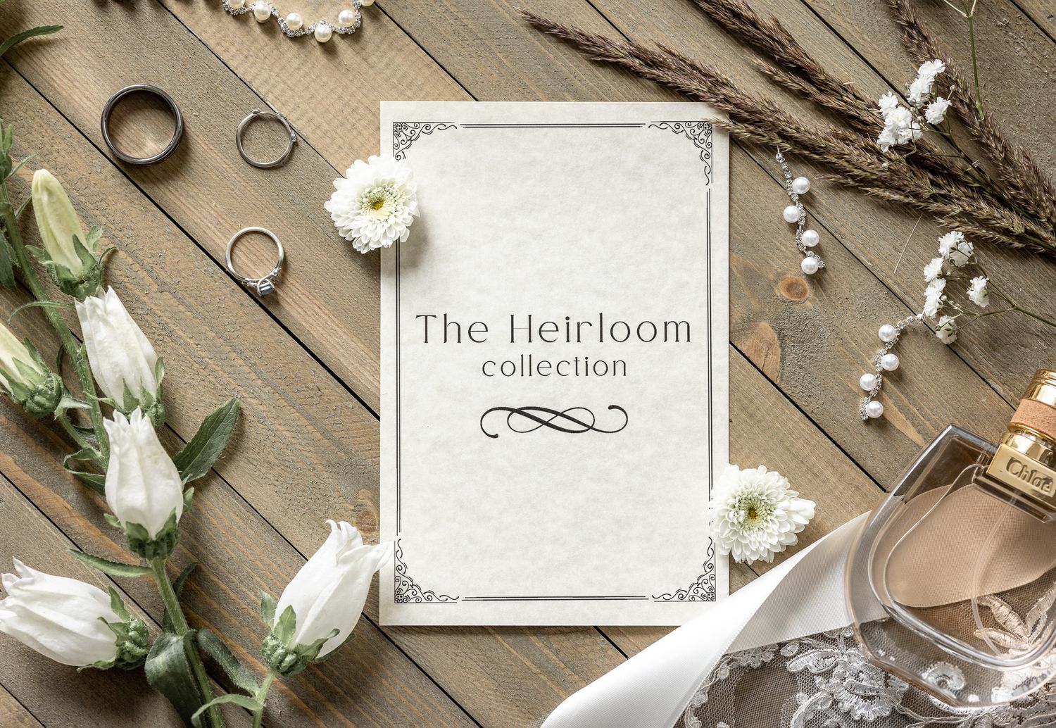 Wedding rings, white roses, and decorative elements arranged on a rustic wooden surface with an heirloom collection card.