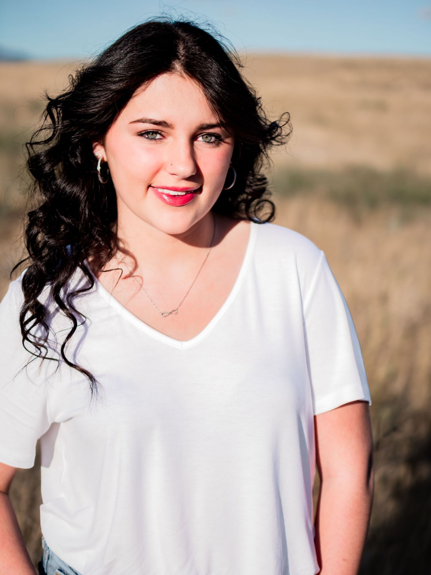 A casual portrait of someone in a white v-neck shirt against a golden outdoor background.
