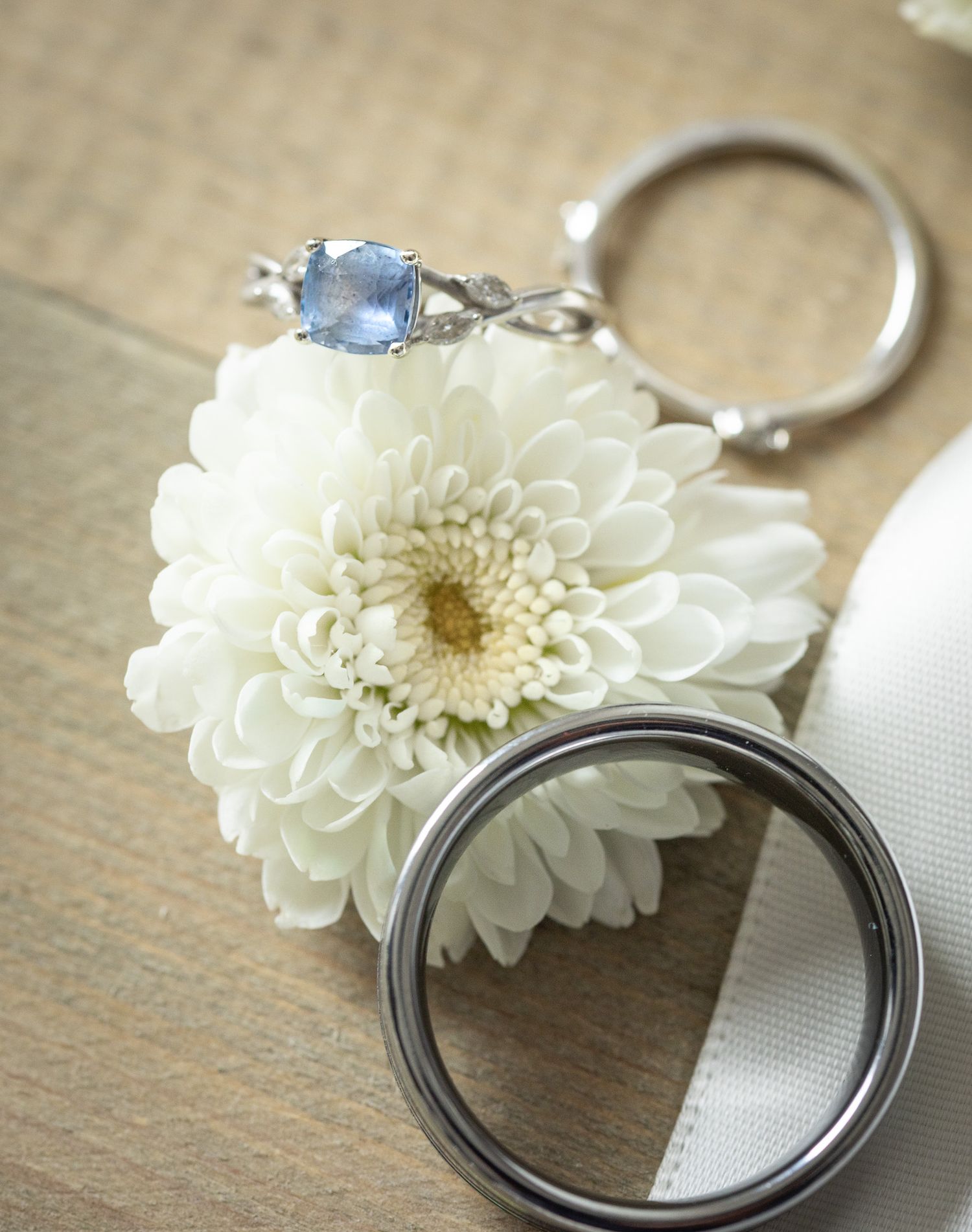 A white chrysanthemum flower placed on a rustic wooden surface with a silver ring beside it.