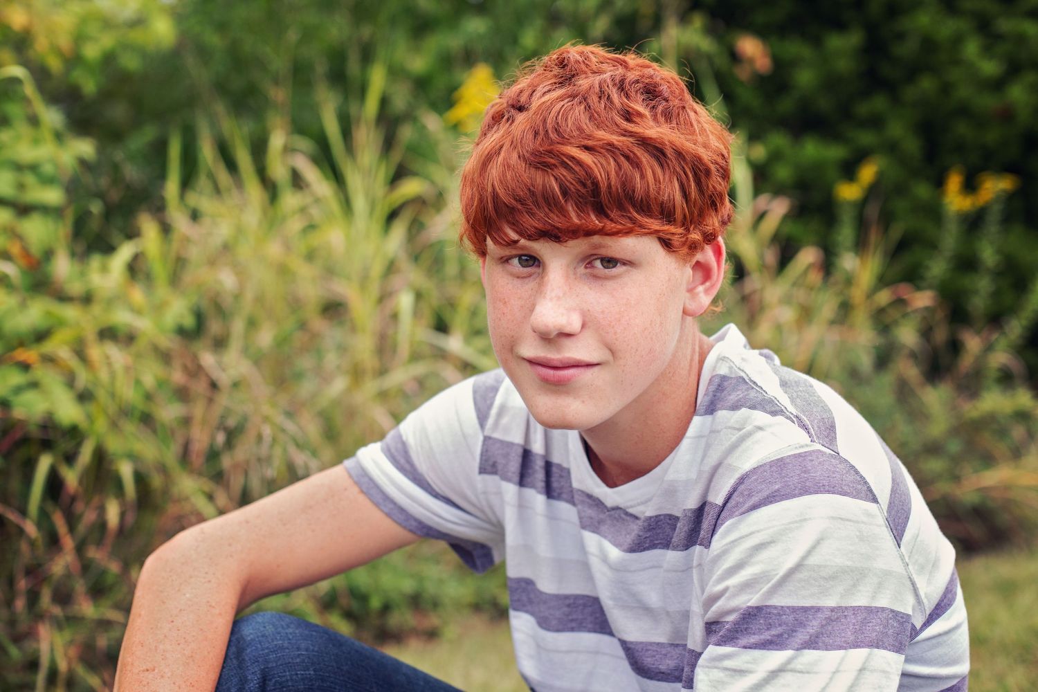 A person in a striped shirt sits outdoors against a green garden background during summer.