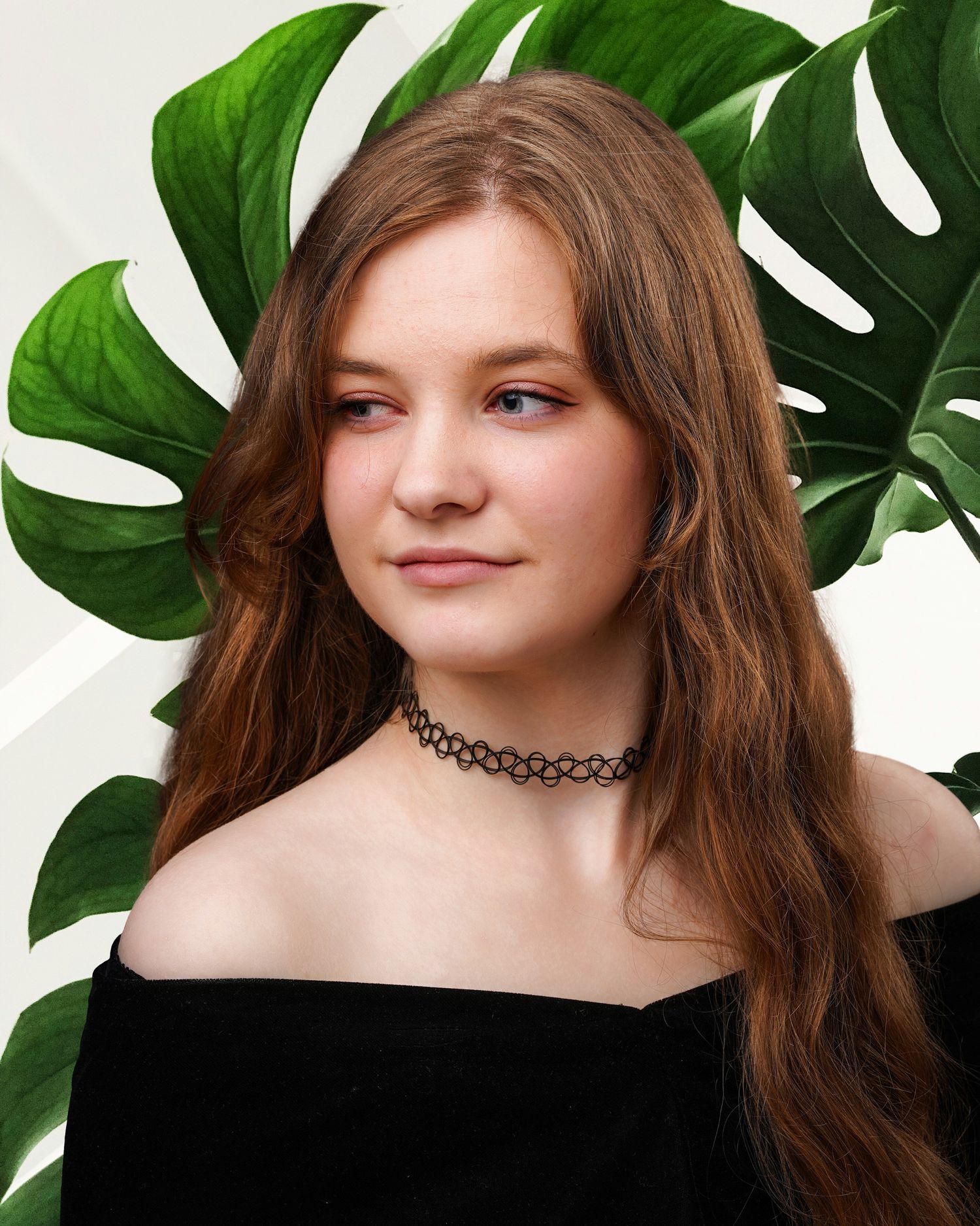 A portrait against a monstera leaf backdrop shows a person in a black off-shoulder top with brown hair and a choker necklace.