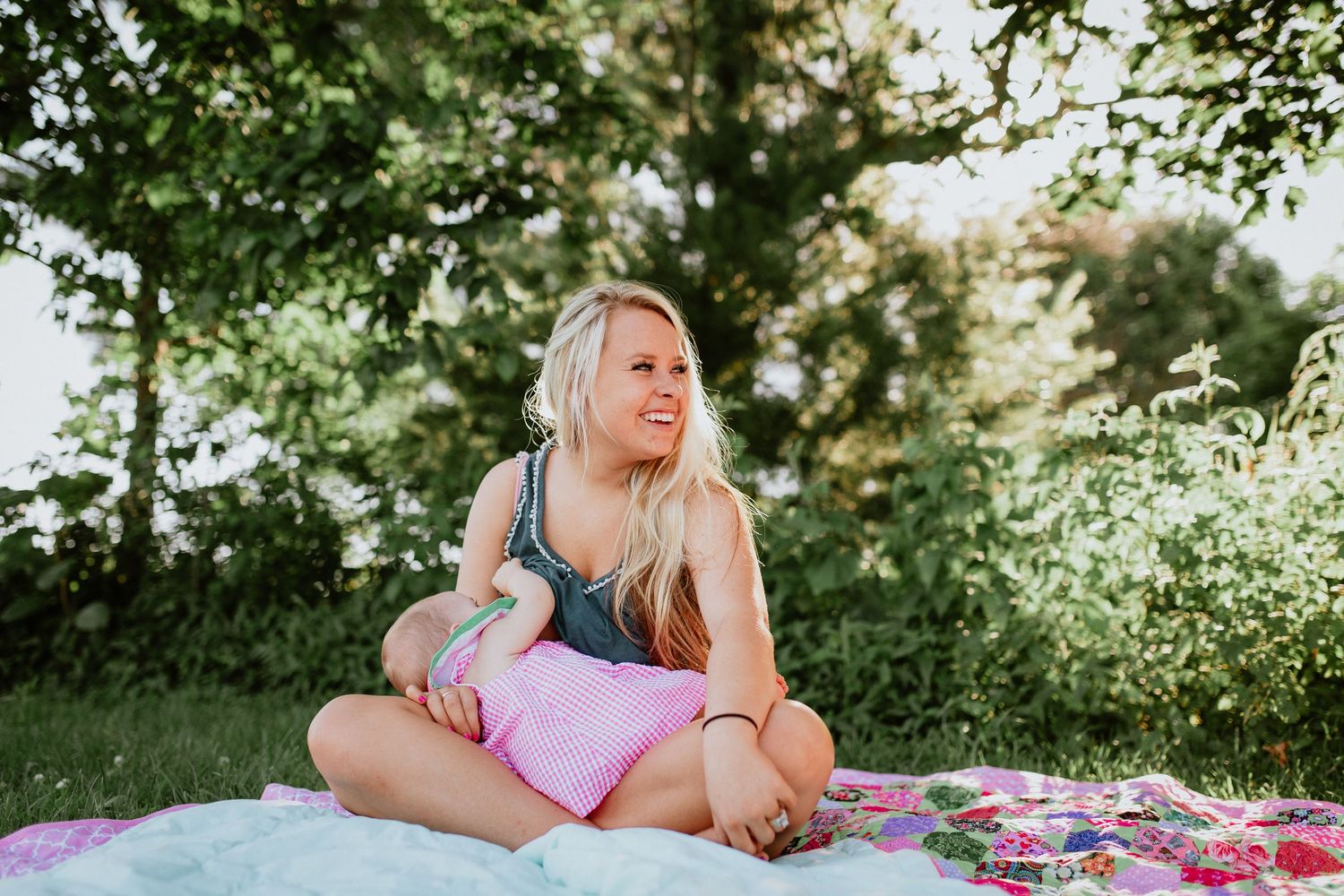 A couple lying on a colorful blanket in a sunny park shares a tender moment together.
