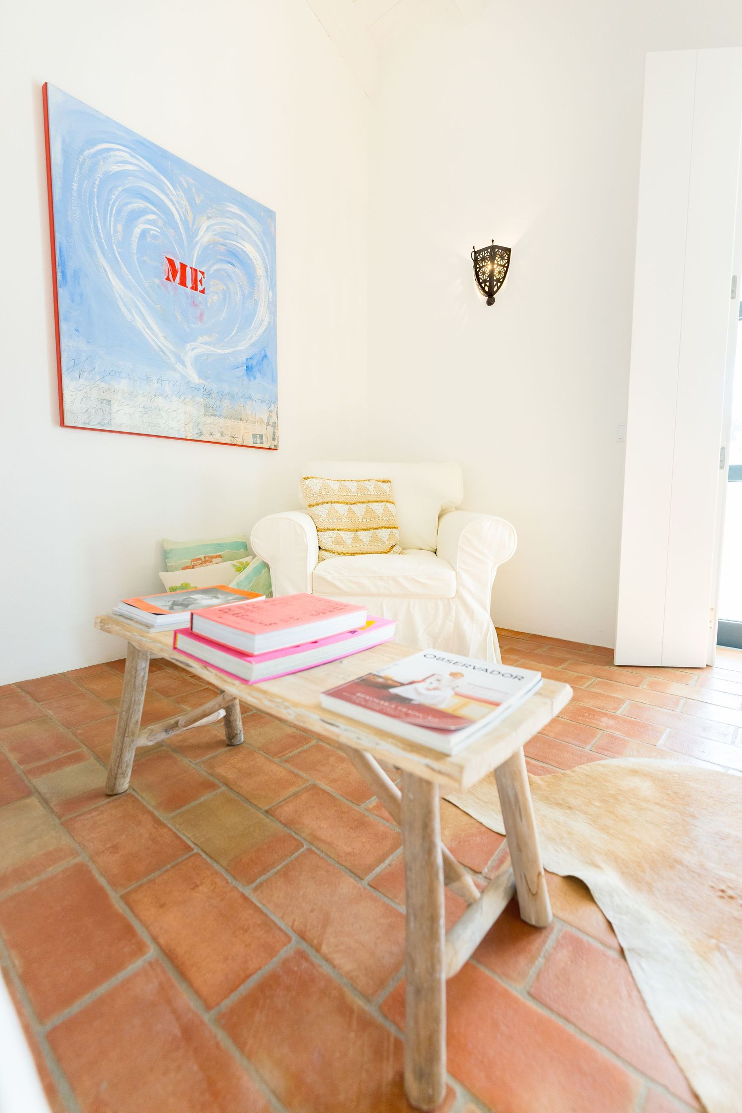Cozy reading nook with white armchair, wooden bench, and blue heart artwork.