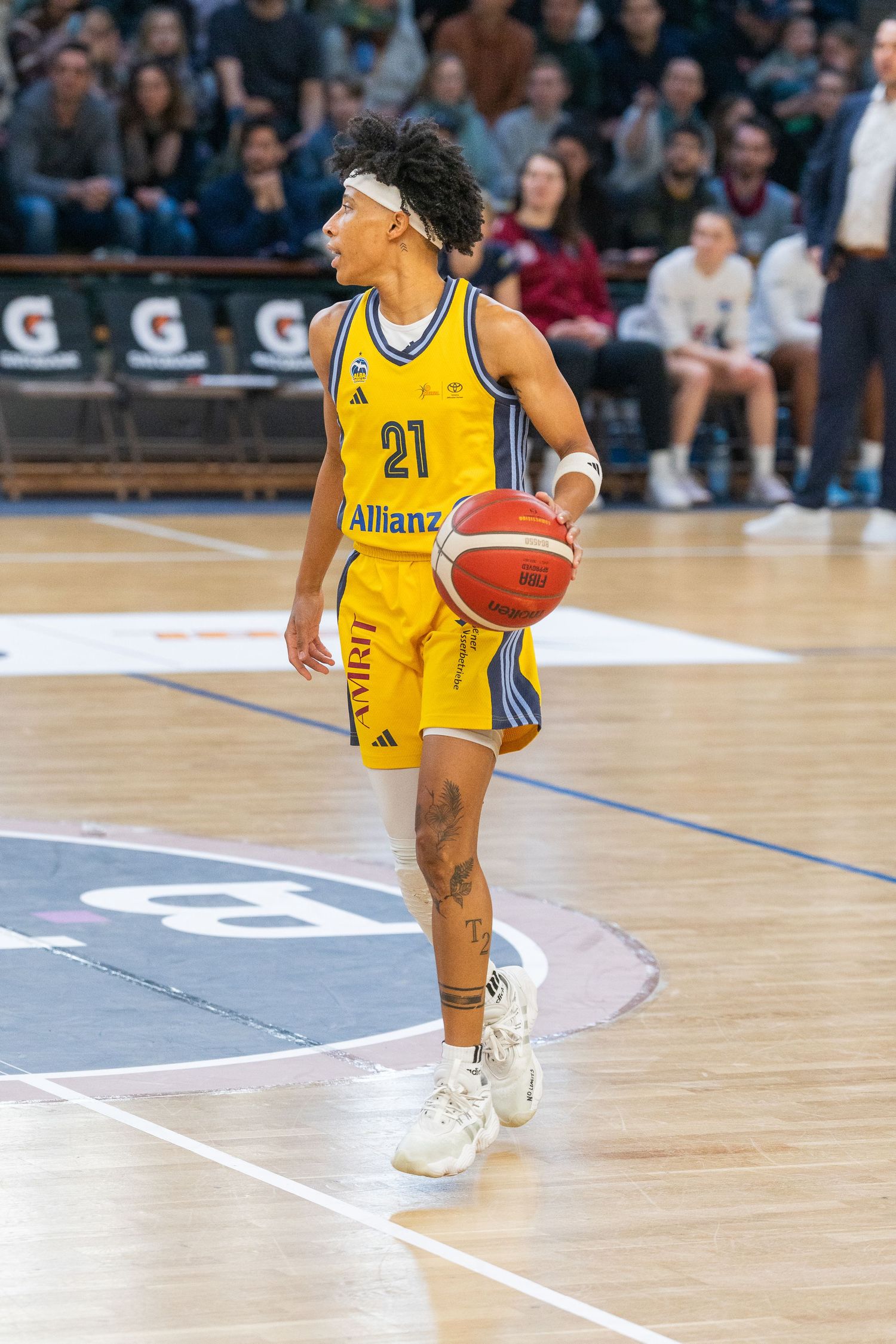 Basketball player in yellow Allianz jersey number 21 dribbles ball on court during professional game.