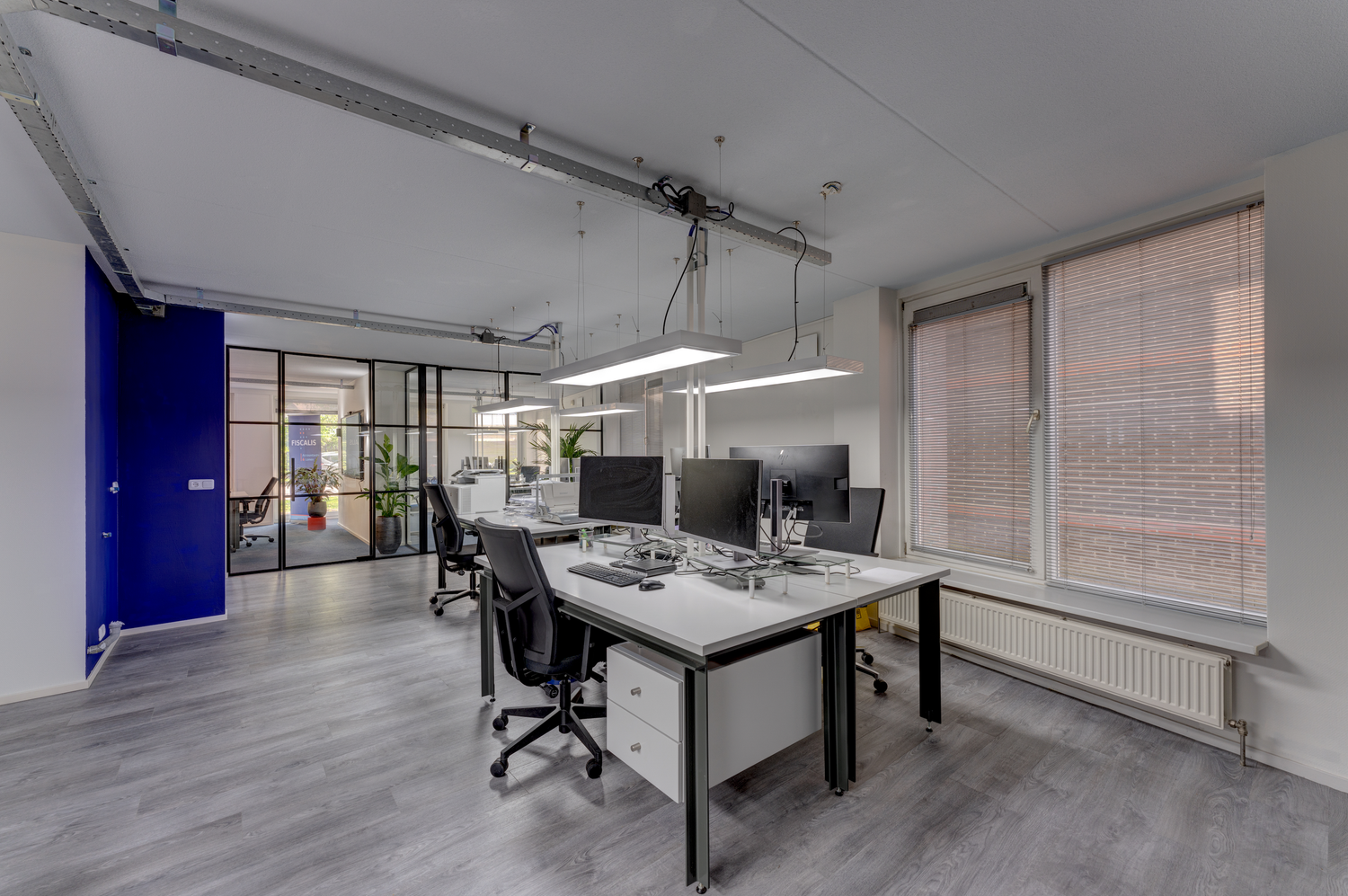Modern office workspace with white desks, office chairs, and blue accent wall in an industrial-style setting.