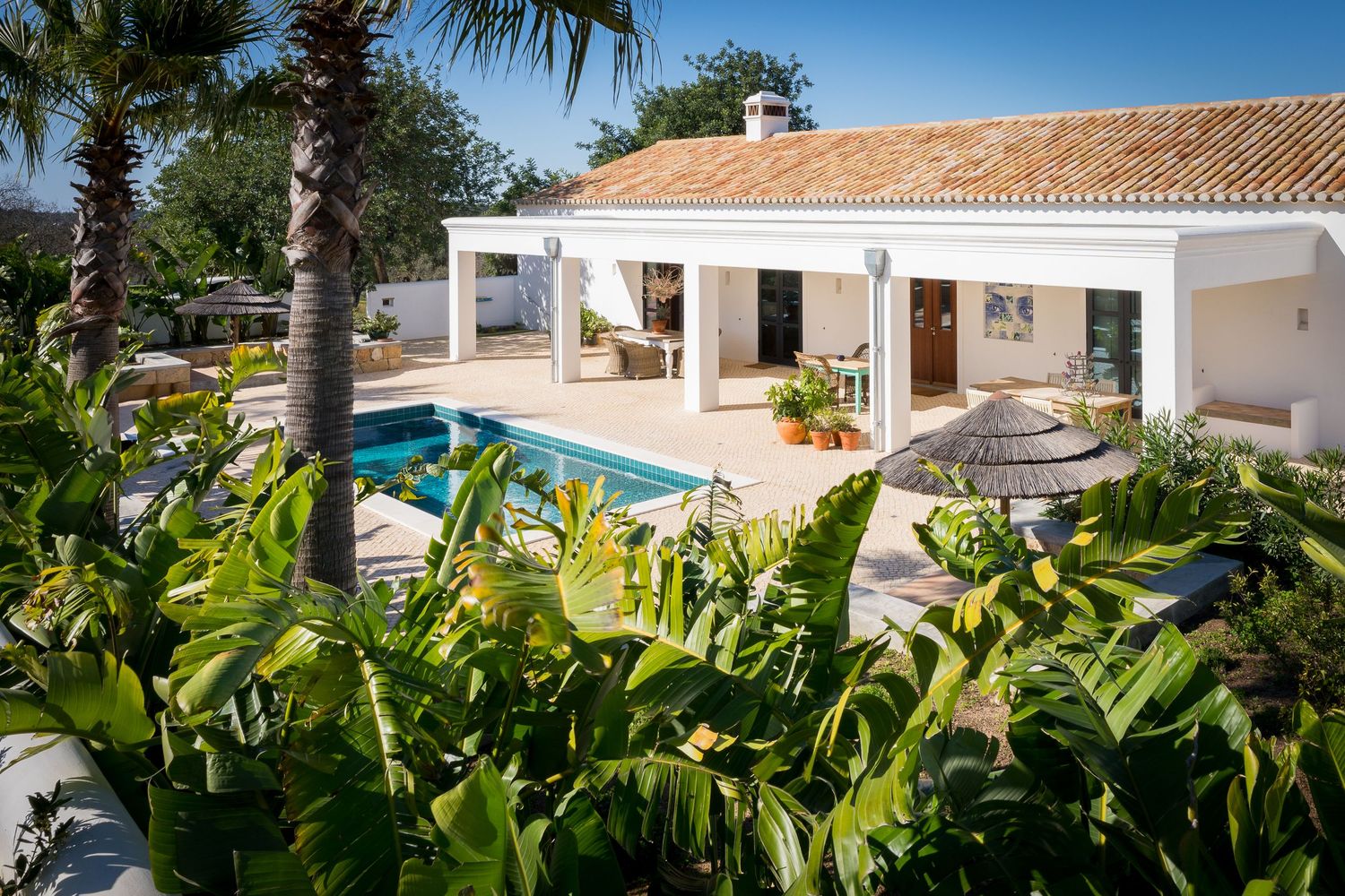 Mediterranean villa exterior with swimming pool, palm trees, and covered patio area.