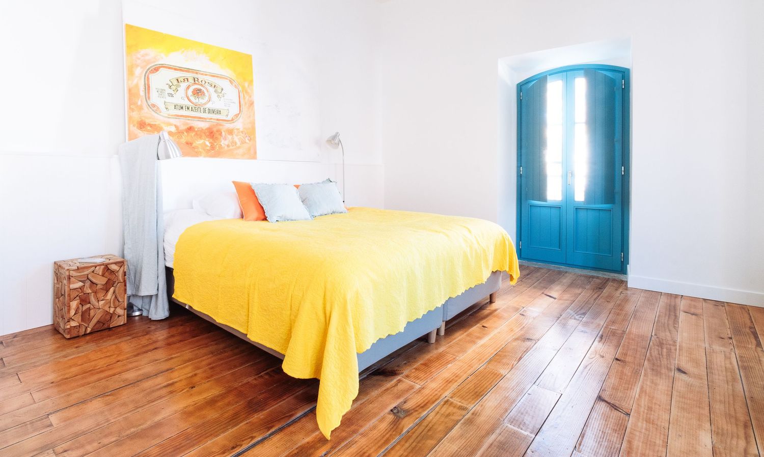 Bright bedroom with wooden floors, yellow bedding, and a turquoise blue door.