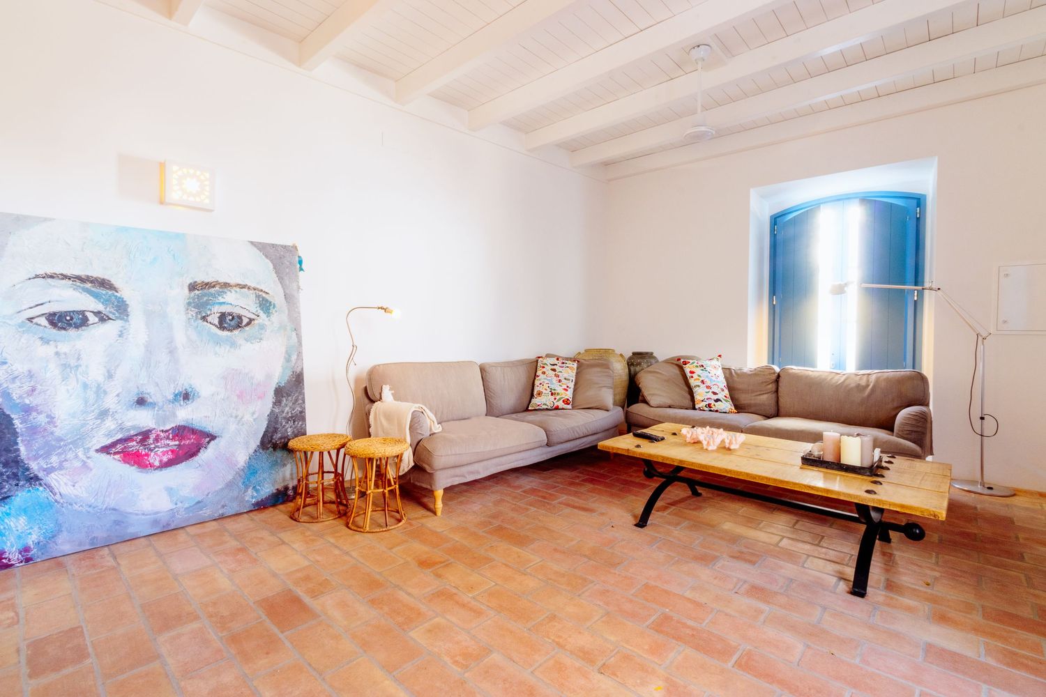 Modern living room with terracotta floors featuring a gray sectional sofa and large artistic portrait on the wall.