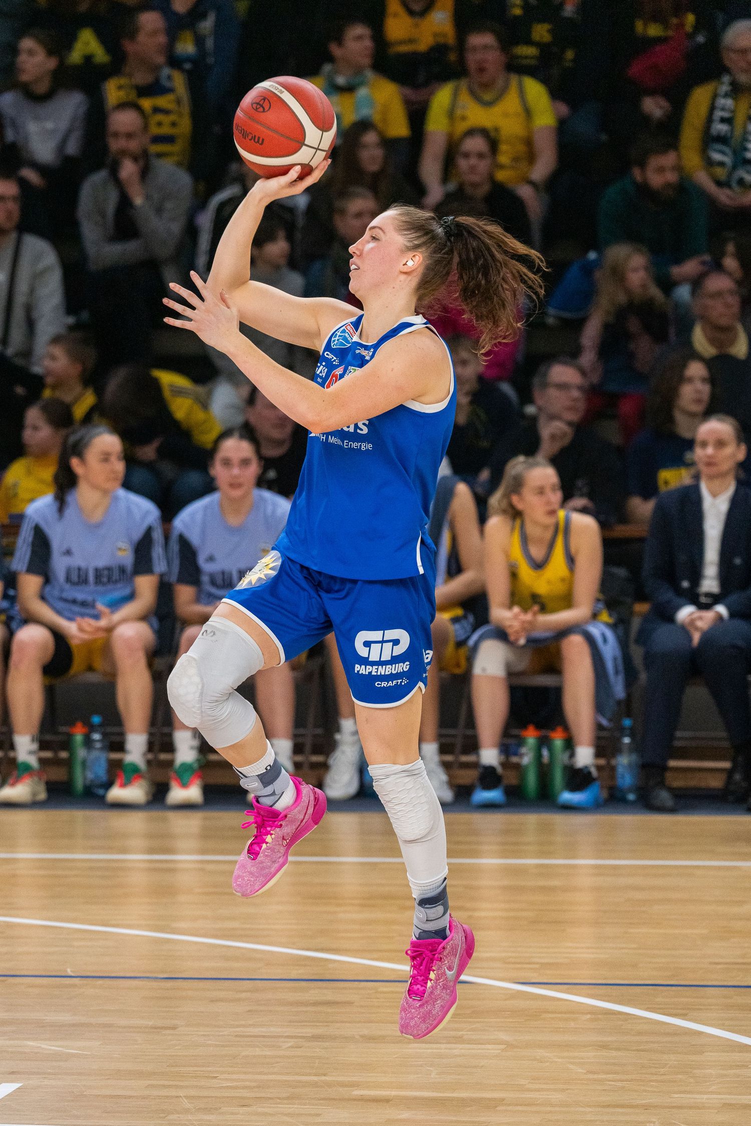 Basketball player in blue jersey and pink shoes leaps to make a shot during an intense game.