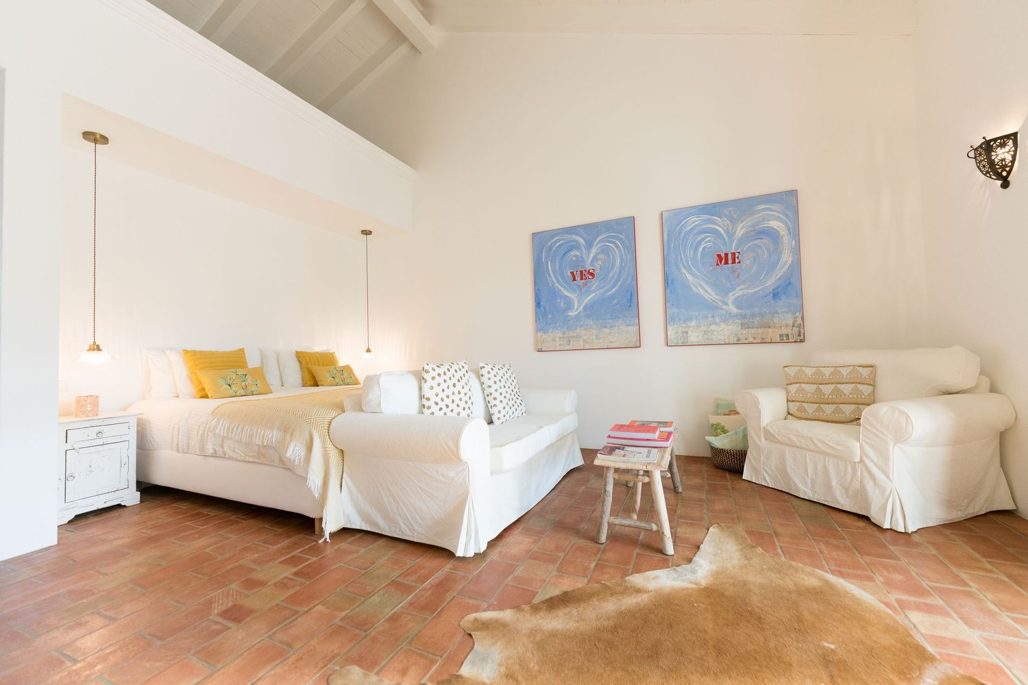 Bright bedroom with two white beds, blue wall art, and terra cotta floors.