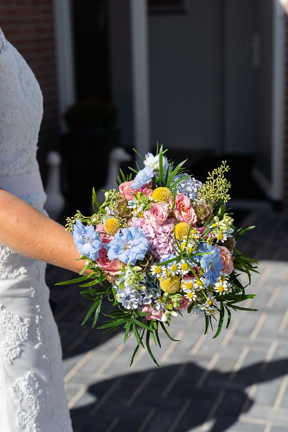 Colorful wedding bouquet with hydrangeas, roses and yellow flowers held against white dress.