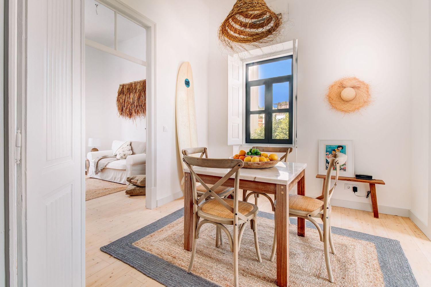 Cozy dining nook with woven decor, surfboard, and natural light from window.