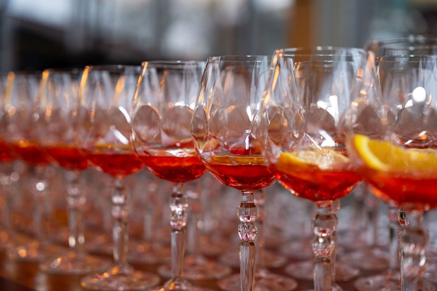 Rows of elegant wine glasses filled with red cocktails and orange citrus garnishes arranged for service.