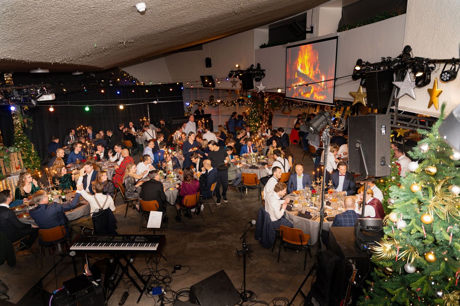 A crowded venue with piano and Christmas tree during a live performance shows audience enjoying holiday entertainment.