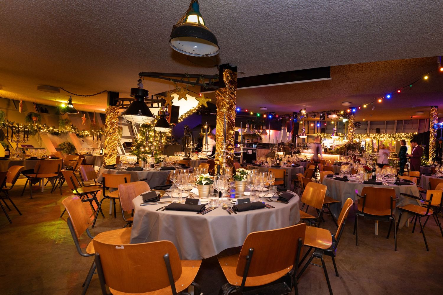 Elegant banquet hall setup with round tables, wooden chairs, and decorative lighting for an evening event.