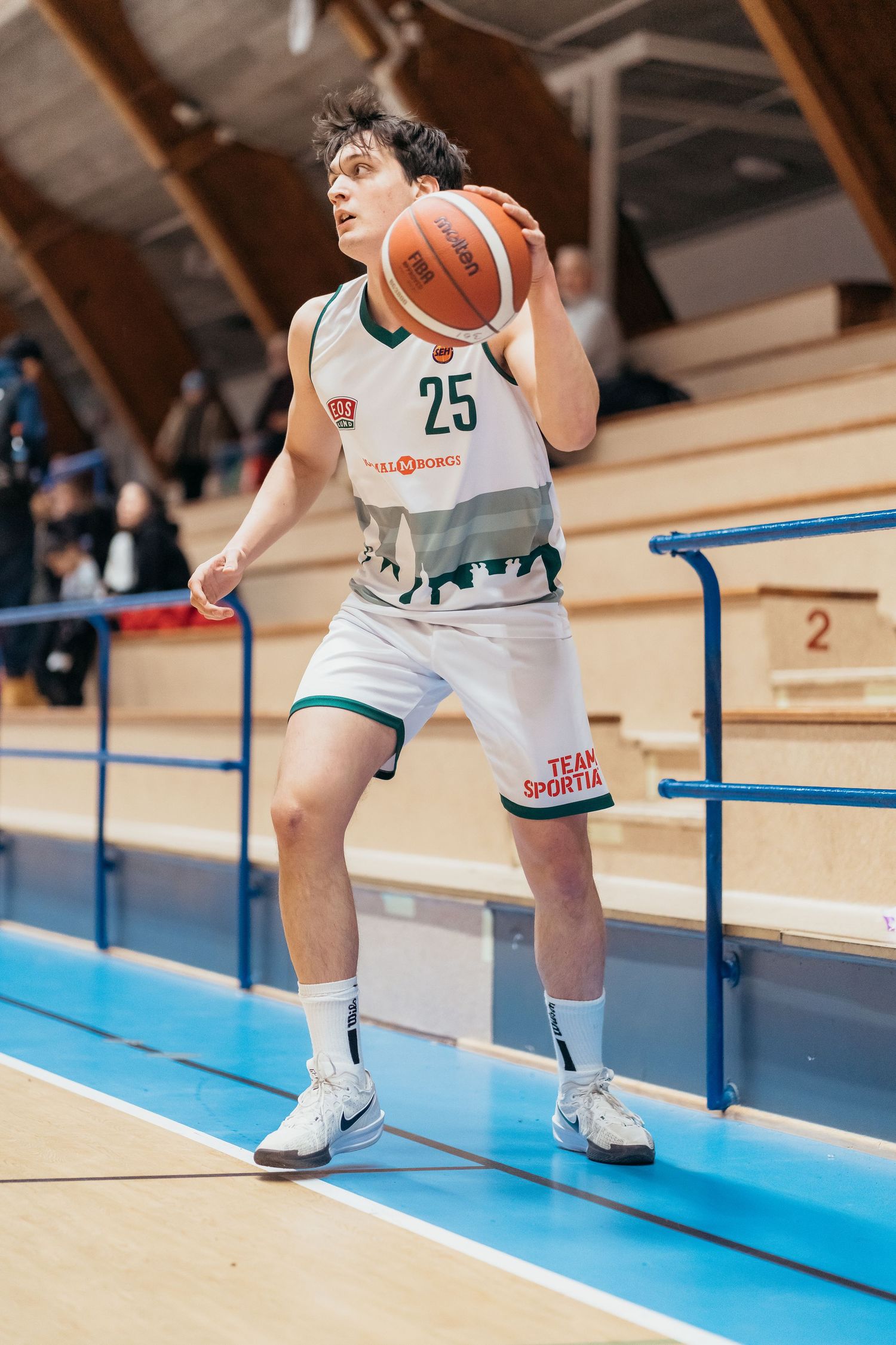 Basketball player in white uniform number 25 holds ball near sideline during indoor game in sports arena.